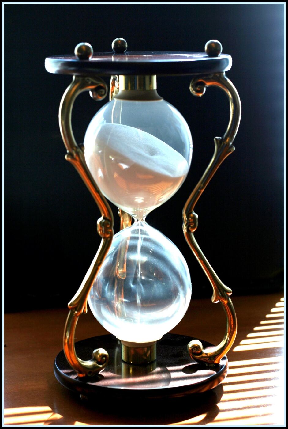Eine Messing-Sanduhr mit rieselndem Sand, von warmem Licht hinterleuchtet